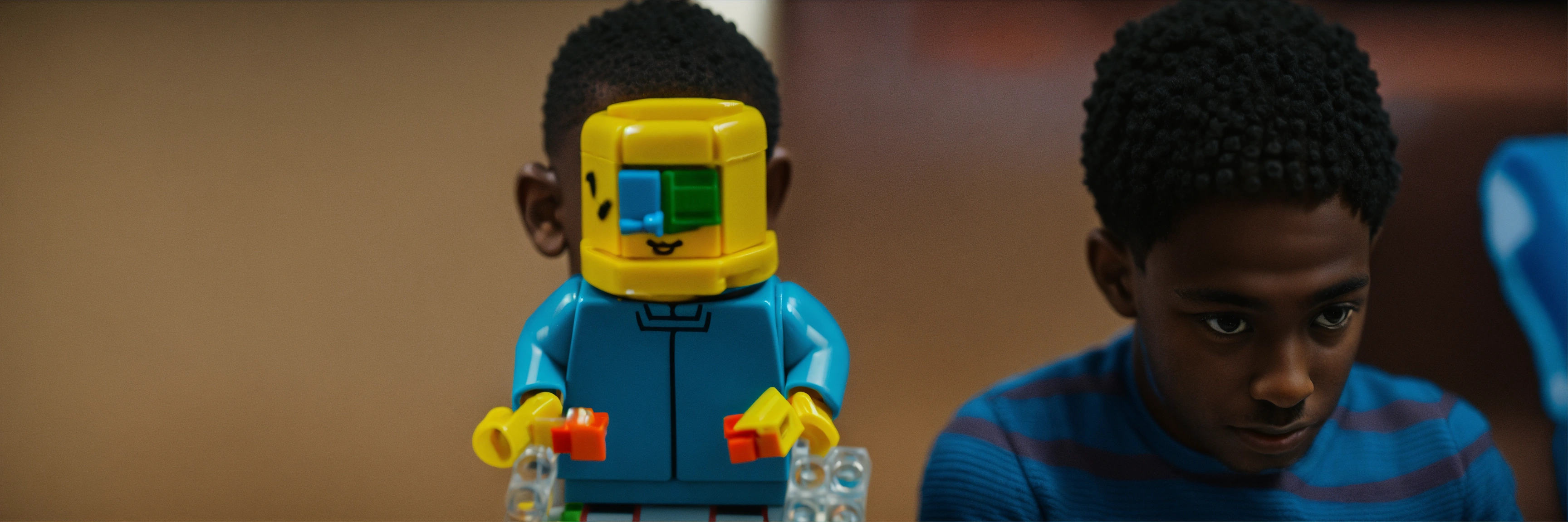 Lexica - A black techy young guy showing a blue piece of lego in his hand.